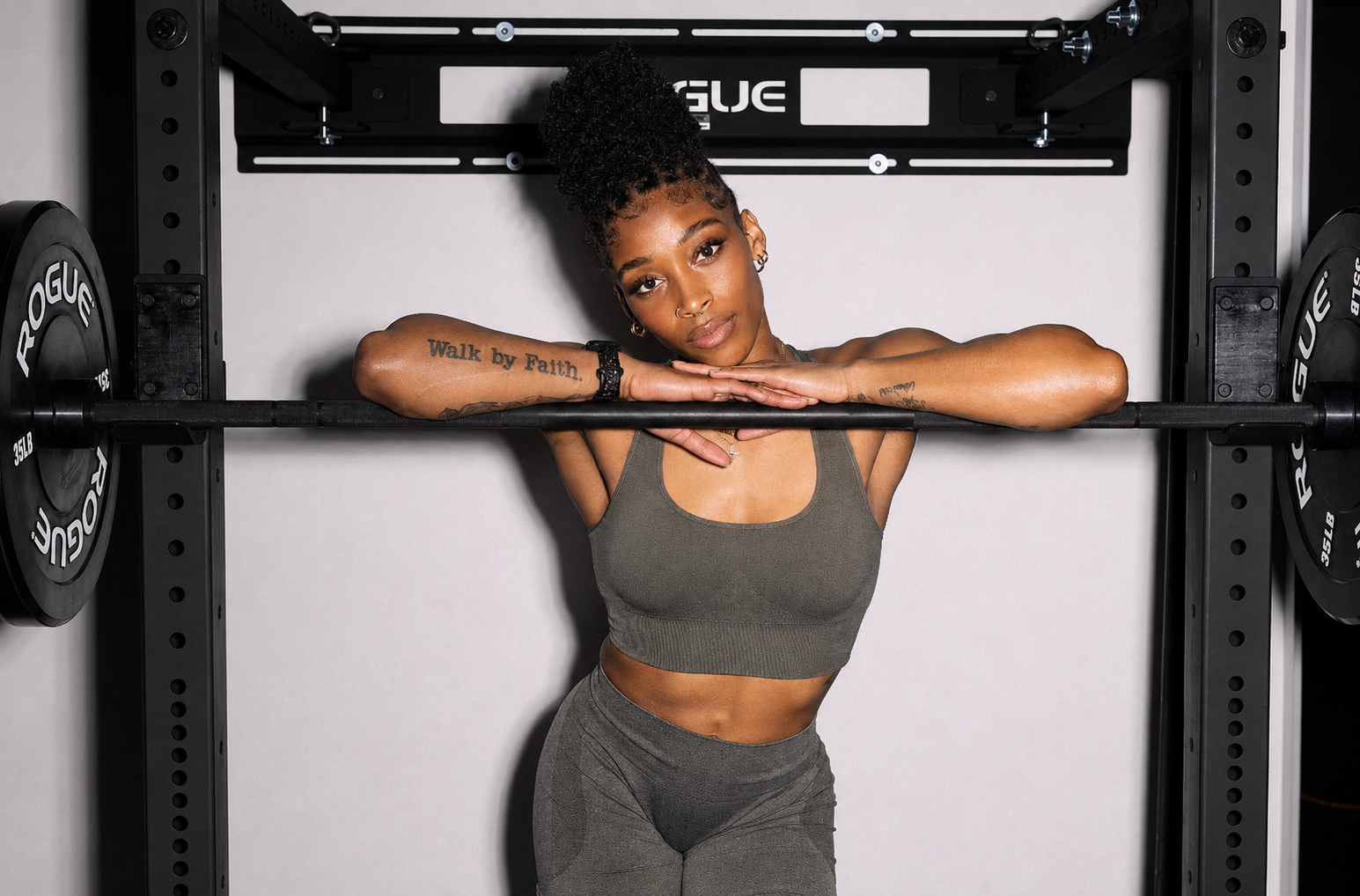Mari resting her head against a loaded barbell in the squat rack